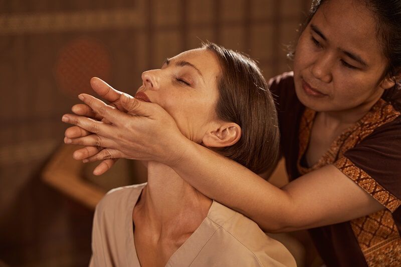 Therapist gently stretching a woman’s neck in a warm, dimly lit spa setting — Leela Thai Massage & Spa in Newtown, QLD