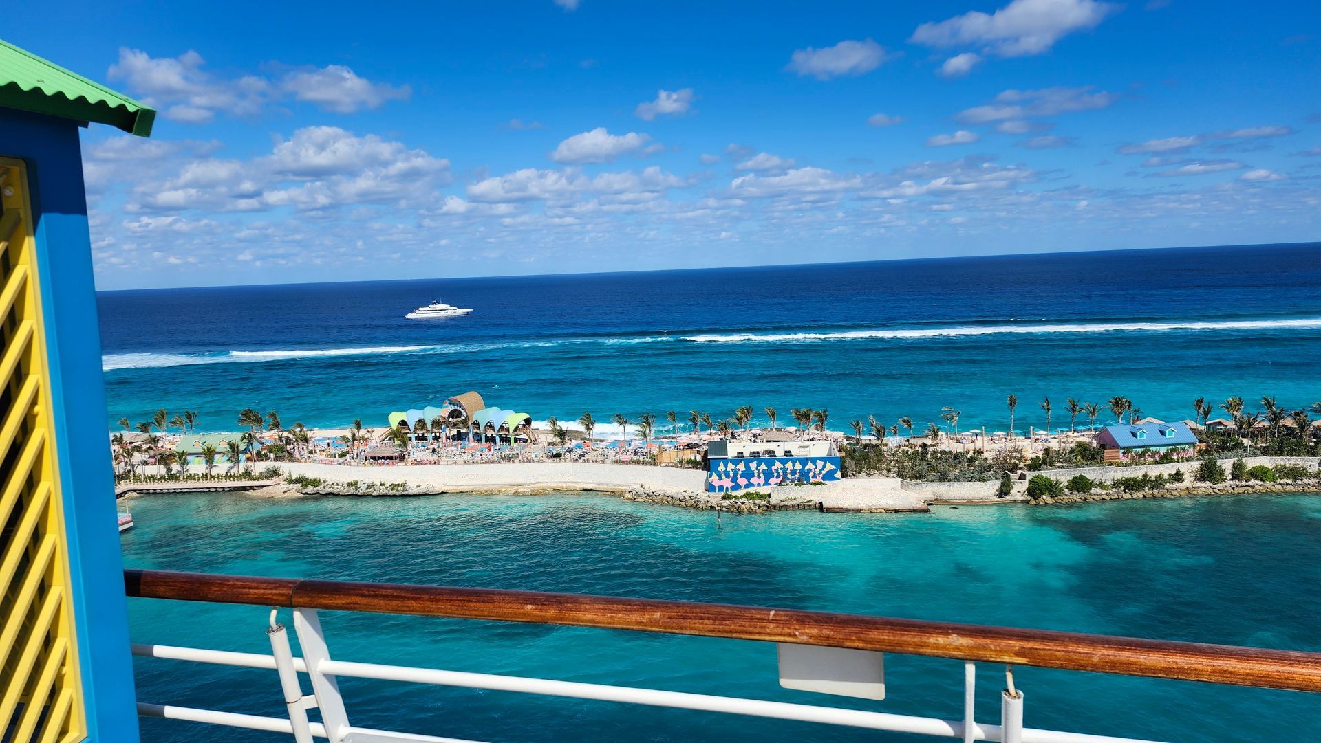 Bright tropical beach with turquoise water, blue sky, and a cruise ship railing in the foreground
