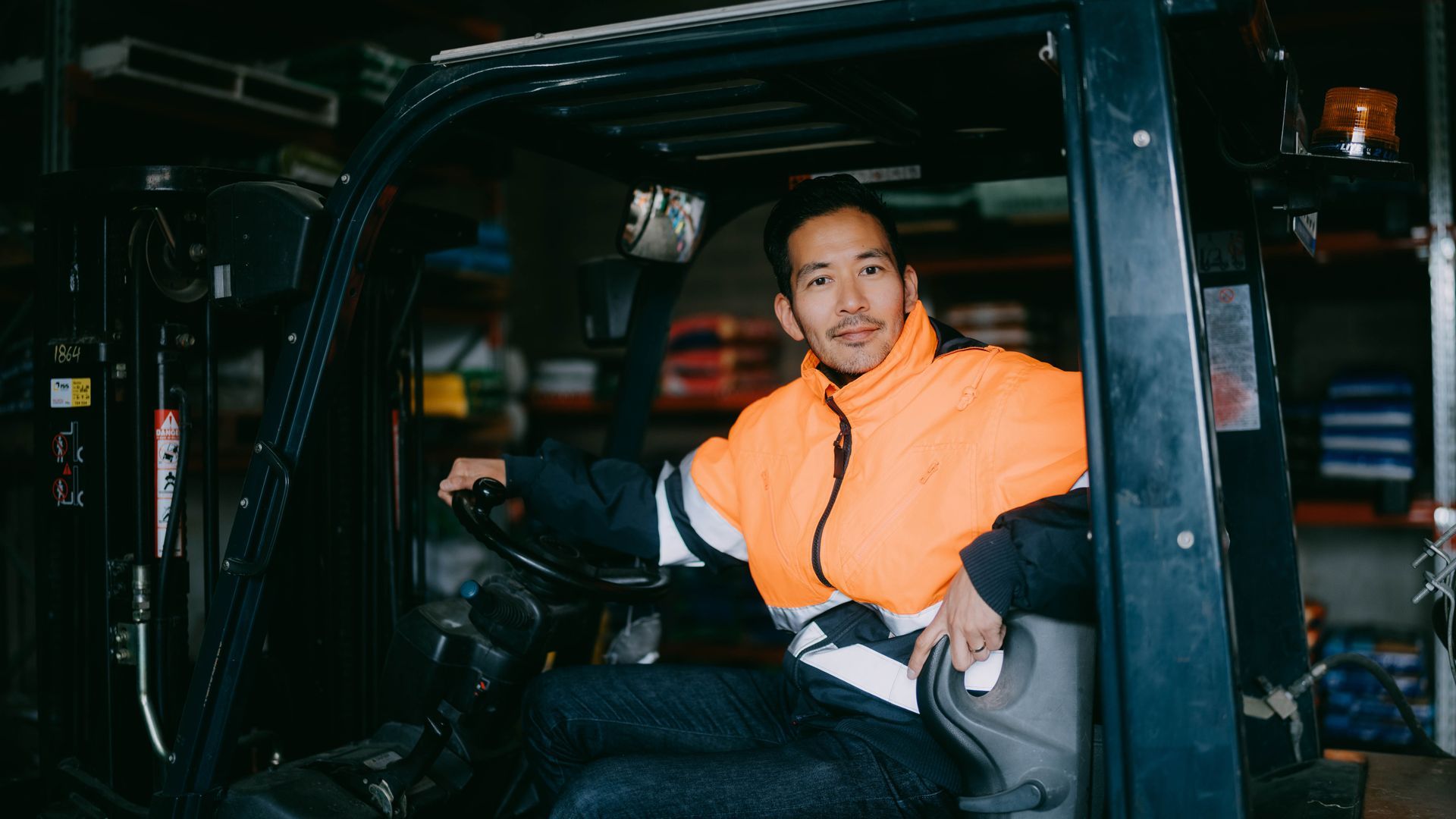 Person in a bright orange jacket seated inside a vehicle interior, looking toward the camera.