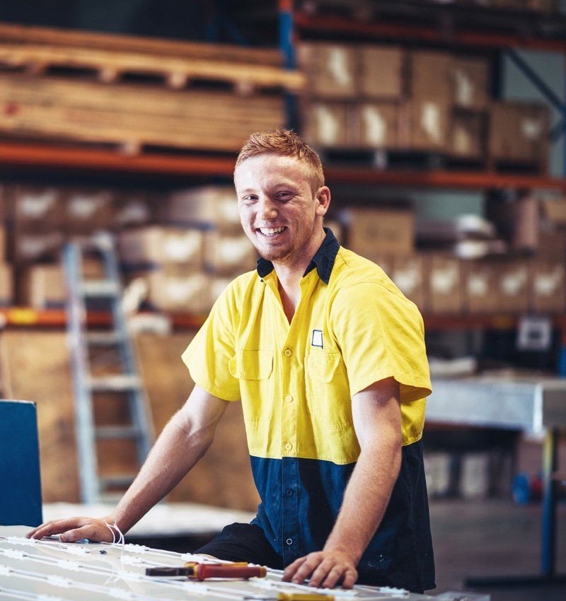 Man in yellow and blue work shirt smiles in a warehouse.