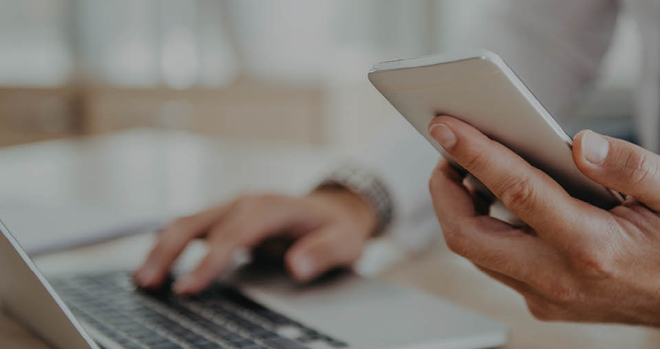 Person using laptop and holding a smartphone, blurred background.