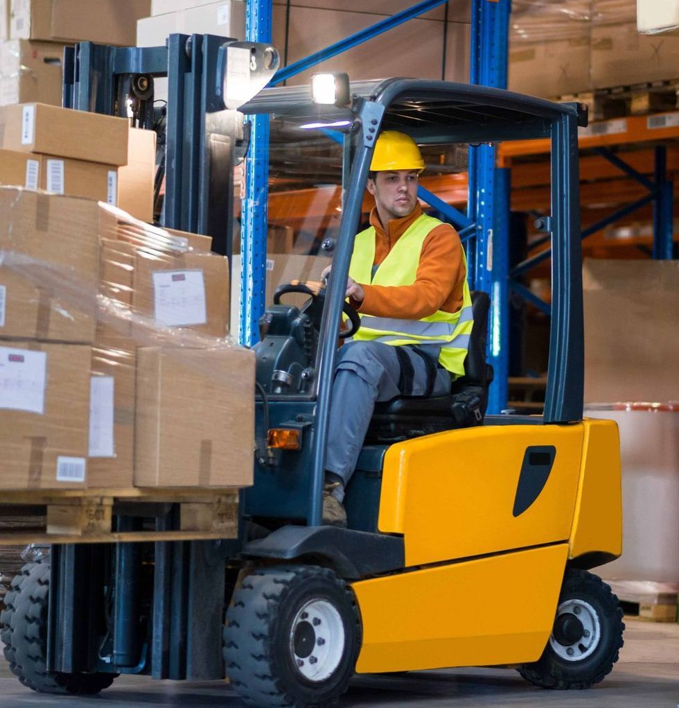 Man in a forklift in a warehouse moving boxes on a pallet.