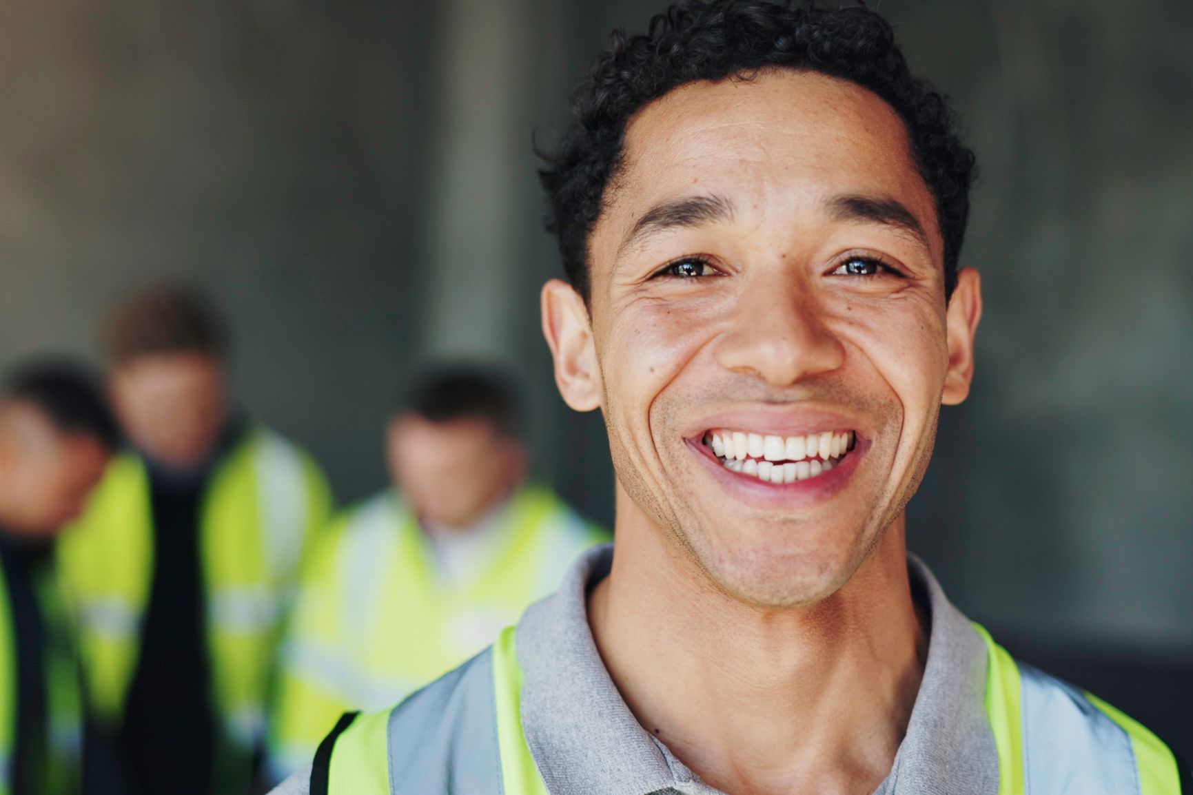 Smiling worker in a reflective vest with blurred colleagues in the background.
