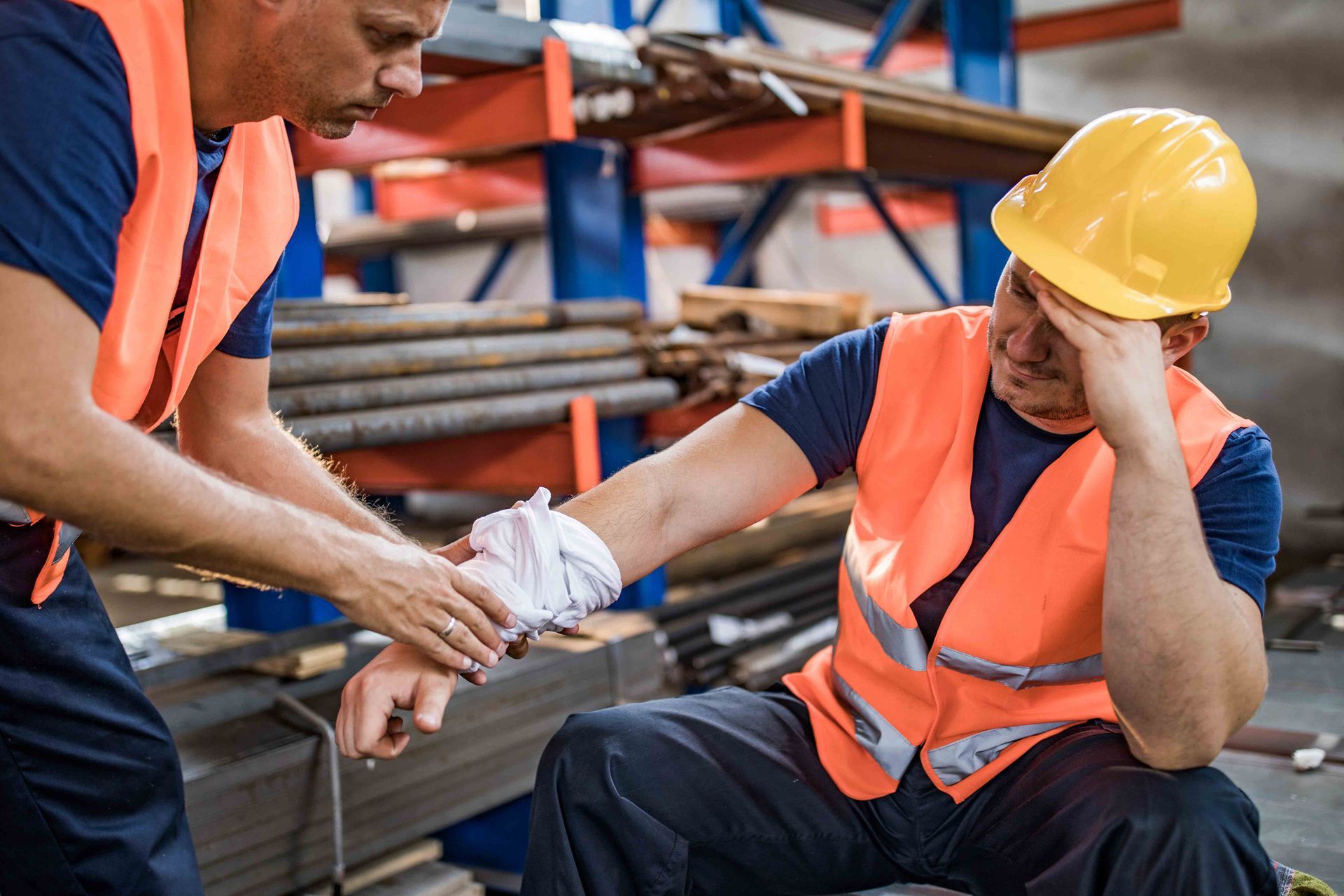 Construction worker with injured arm being helped by colleague in a warehouse.