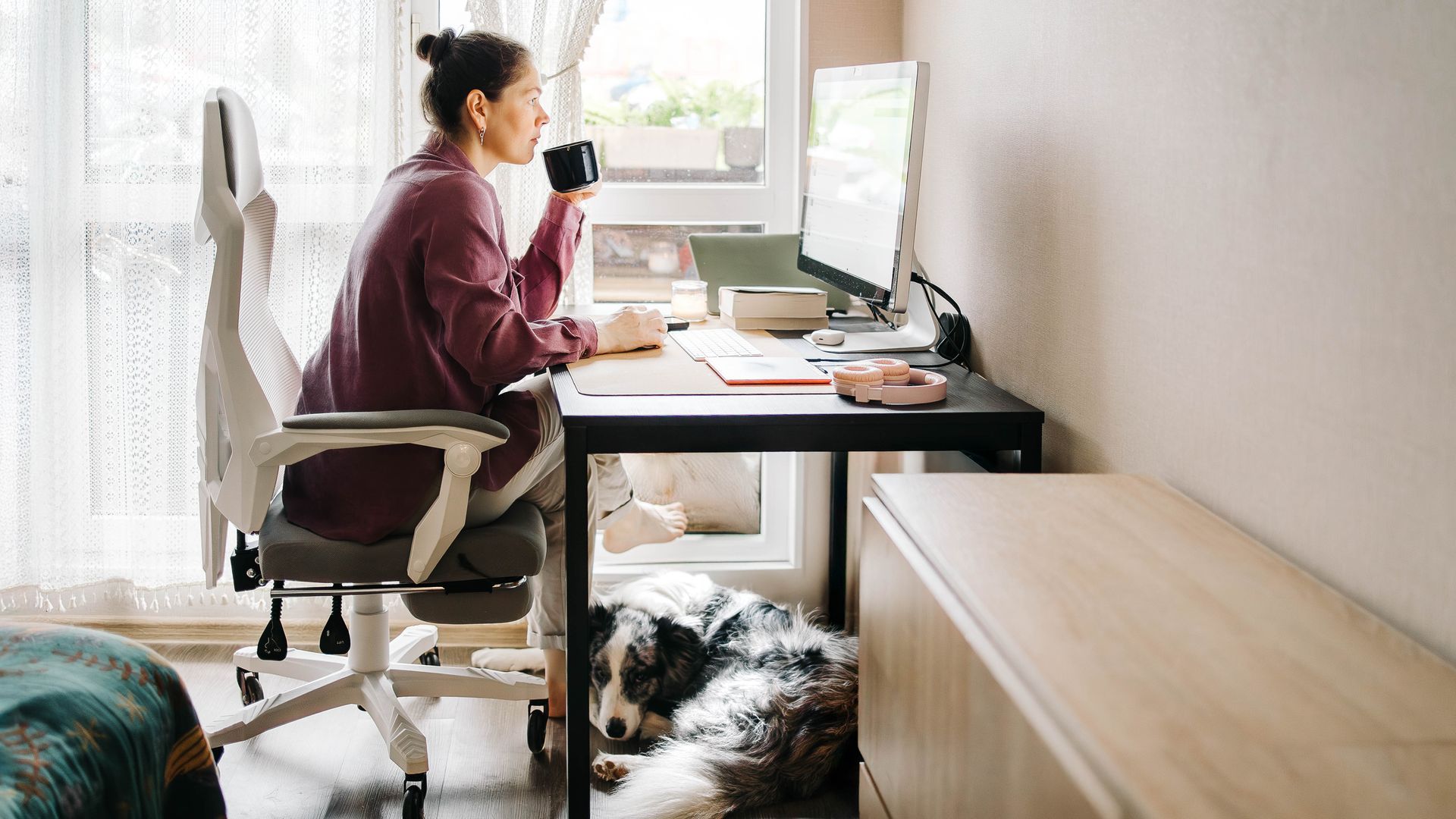 Person working at a desk with dual monitors in a bright home office, using a keyboard and mouse.