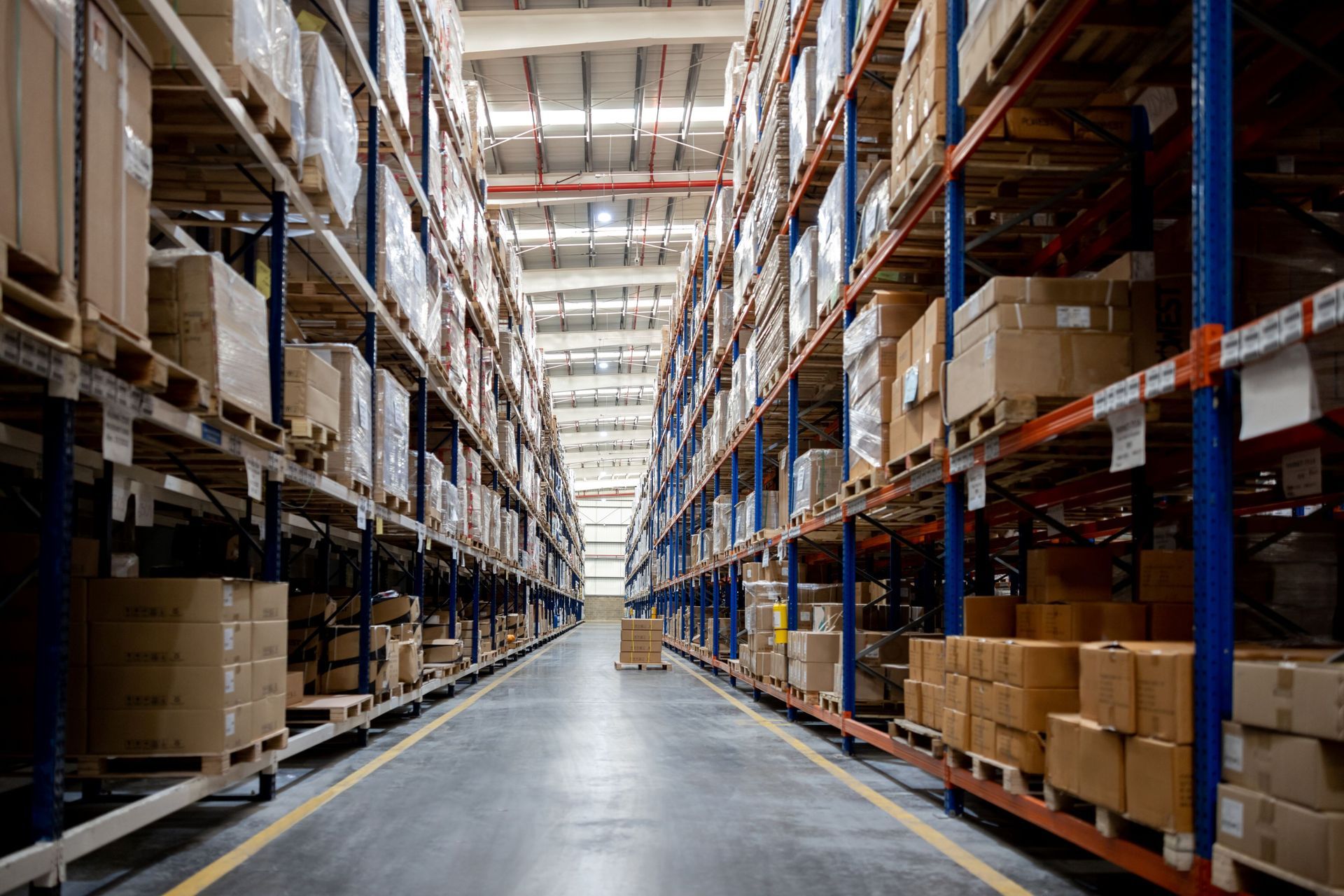 Aisle in a large warehouse with tall pallet racks, stacked boxes, and a polished concrete floor
