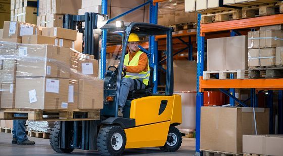 Warehouse worker on a yellow forklift, carrying boxes on a pallet.