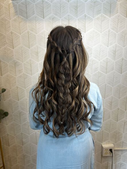 A woman with long curly hair is standing in front of a wall.