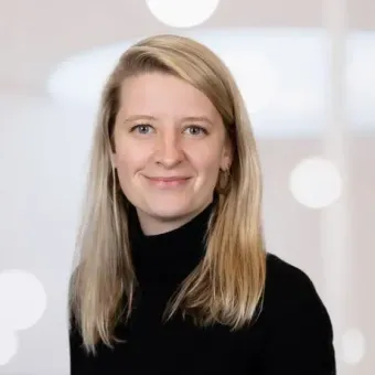 A woman with long blonde hair is wearing a black turtleneck and smiling.
