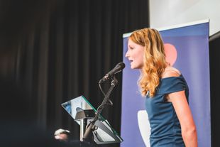 A woman is standing at a podium speaking into a microphone.