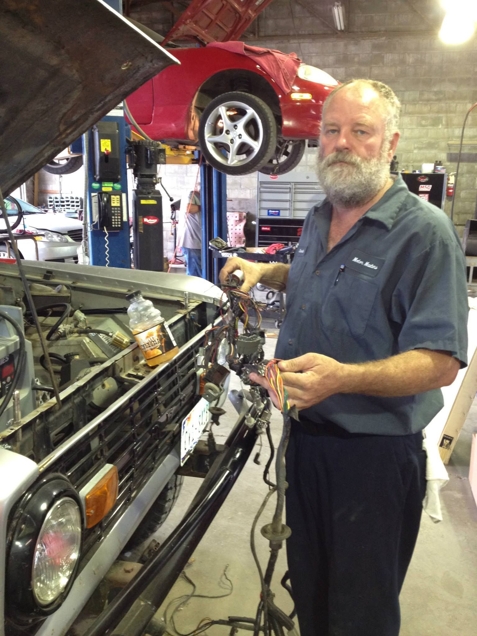 Mechanic holding tools beside a classic car with its hood open in an auto repair shop