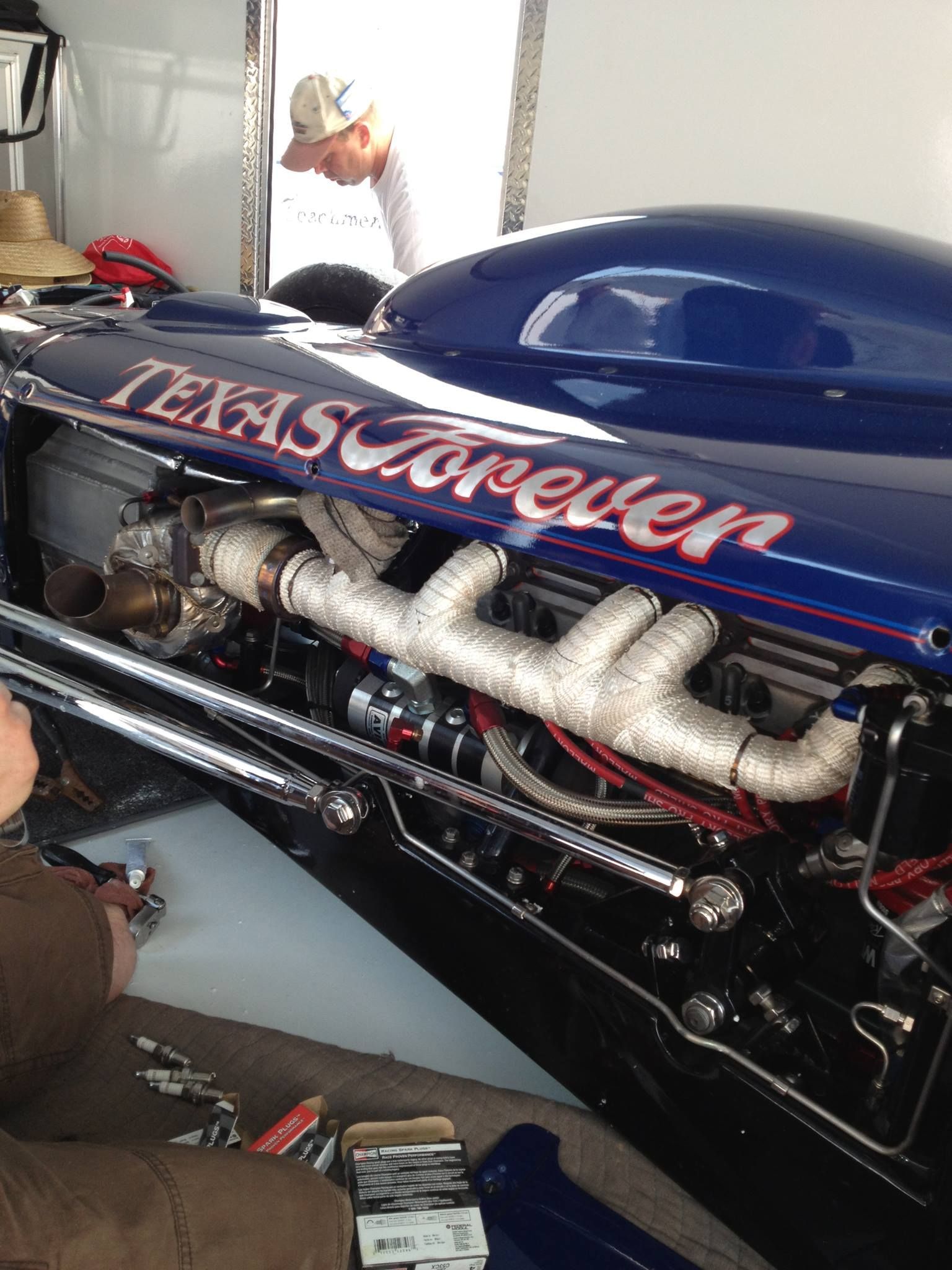 Blue custom hot rod engine with “Texas Forever” lettering and chrome exhaust pipes under the hood