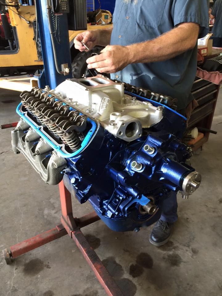 Mechanic working on a blue engine block in a workshop, with tools and parts visible