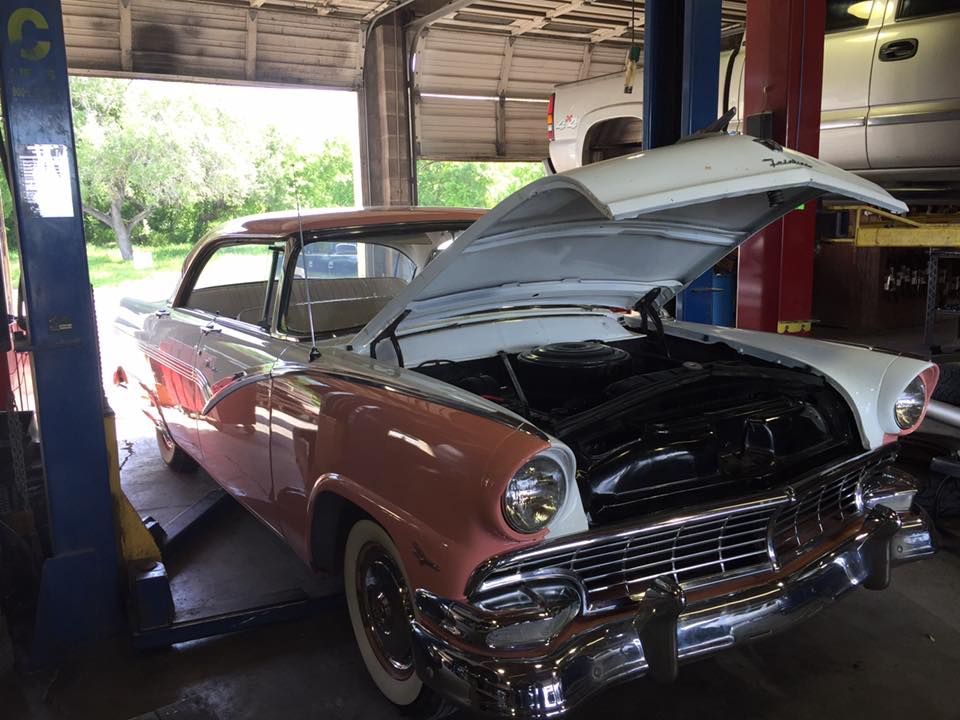 Classic pink and white car with hood open in a garage on a lift