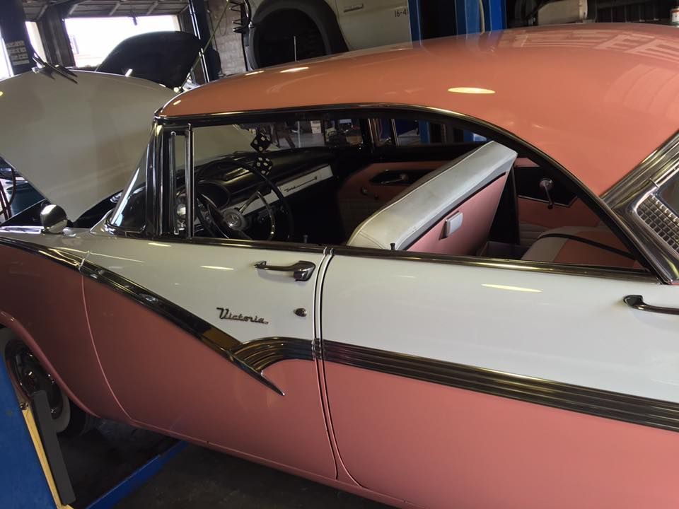 Pink-and-white vintage car at a garage, viewed from the side