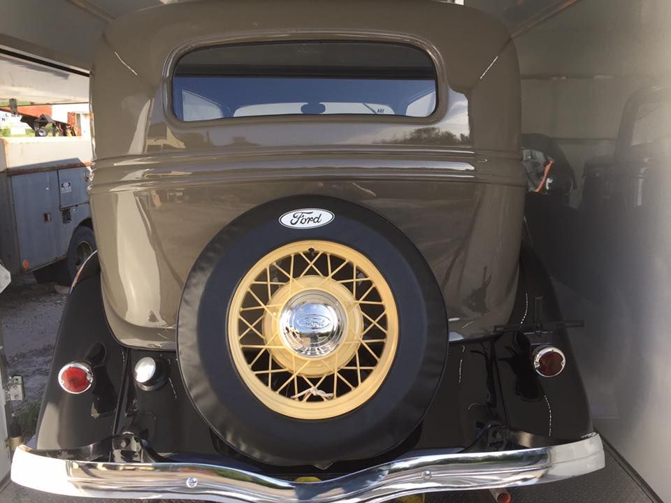 Rear view of a beige vintage car with a spare tire mounted on the trunk.