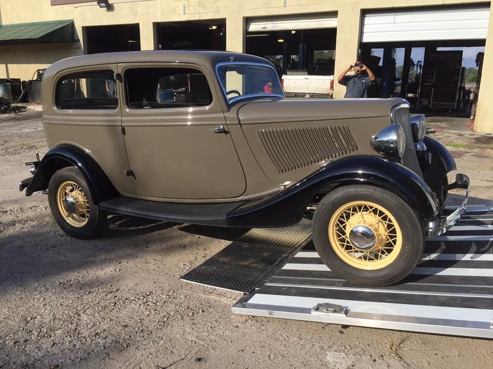 Vintage gray coupe with black fenders and gold wheels displayed outdoors on a striped mat.