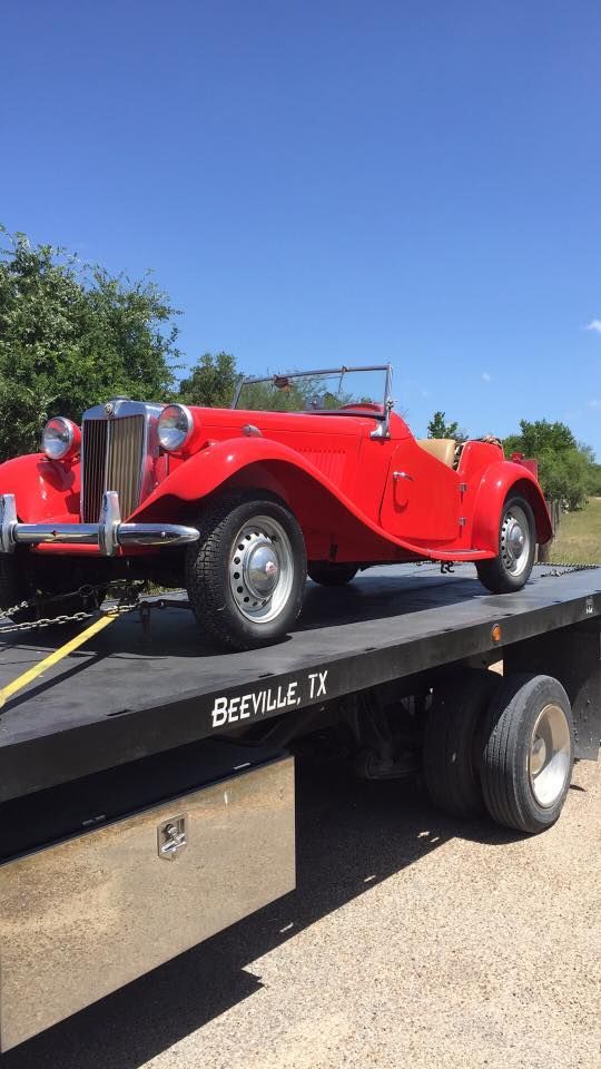 Red vintage convertible sports car on a flatbed trailer outdoors under a blue sky