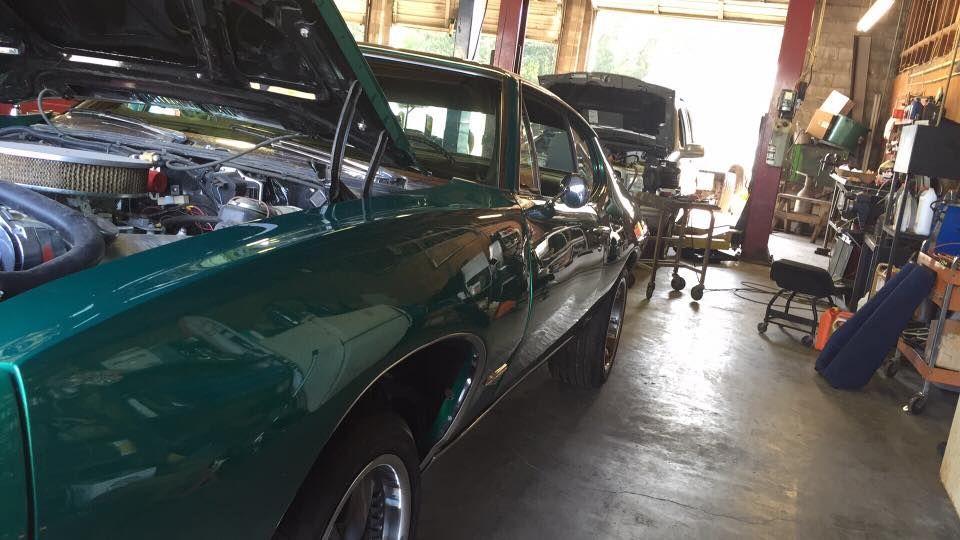 Green classic car in an auto shop garage with its hood open for repair