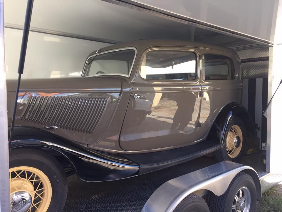 Vintage black classic car on a trailer inside a garage or transport truck.