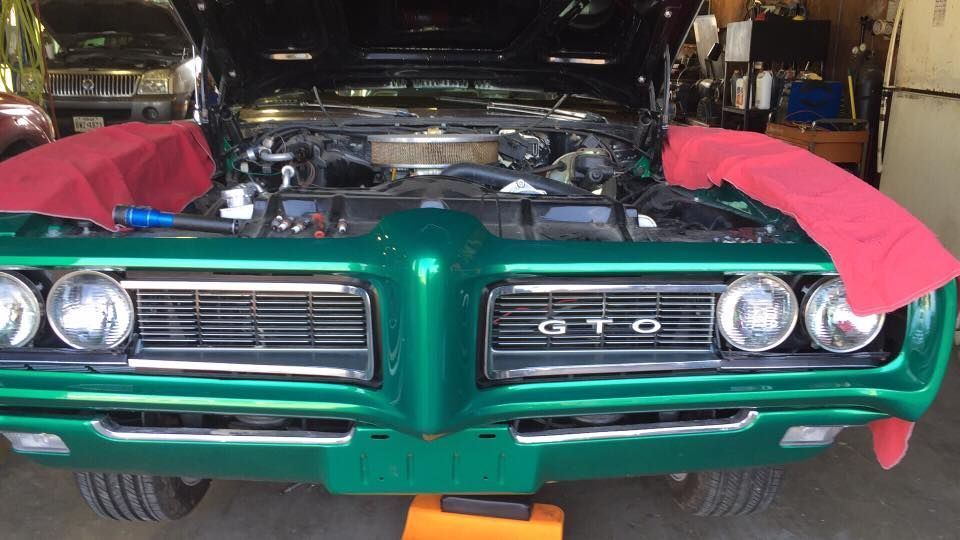 Green Pontiac GTO front view with hood open and red fenders protected in a garage, engine exposed