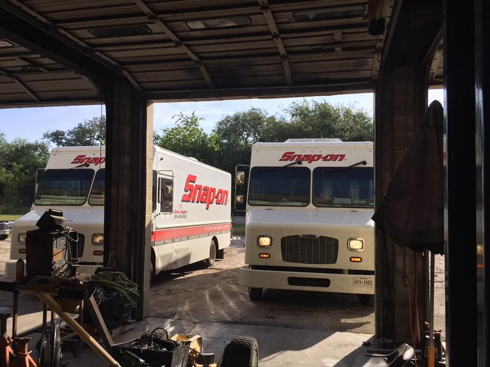 Two white Snap-on trucks parked in a garage bay, with a vehicle lift in the foreground.