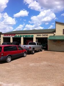 Storefront with parked red SUV and silver pickup under a blue sky with clouds