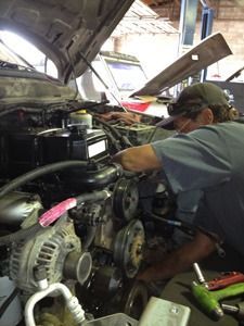 Mechanic working on a car engine in a garage with the hood open