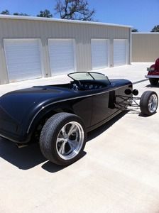 Black hot rod coupe parked beside a white garage on a sunny day