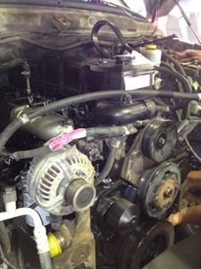 Car engine bay with exposed belts, pulleys, alternator, and hoses under the hood
