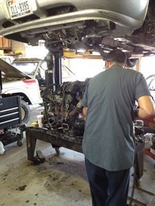 Mechanic working on a car engine at a repair shop, with a lifted vehicle overhead