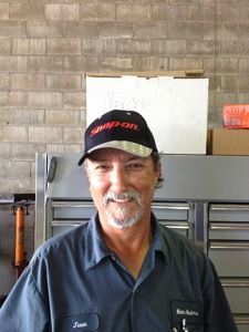Man in navy shirt and black cap standing in front of gray tool cabinets and a concrete block wall