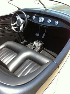 Classic car interior with black leather seats, chrome dashboard gauges, and steering wheel