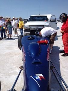 Blue dragster on a salt flat with people gathered around and a white pickup truck behind it.