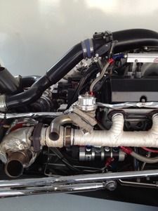Close-up of a vehicle engine bay with black hoses, metal pipes, and a turbocharger.