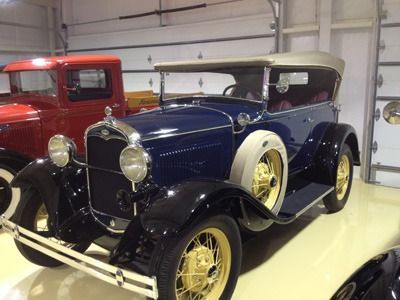 Two vintage cars in a garage, including a blue-and-black convertible with cream wheels in front