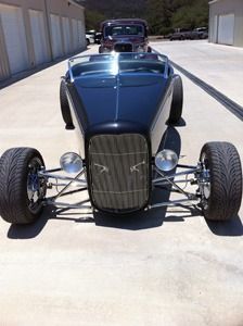 Front view of a blue vintage hot rod with exposed wheels parked on a sunny driveway