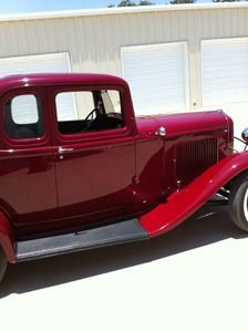 Maroon vintage coupe parked in front of a light-colored garage door