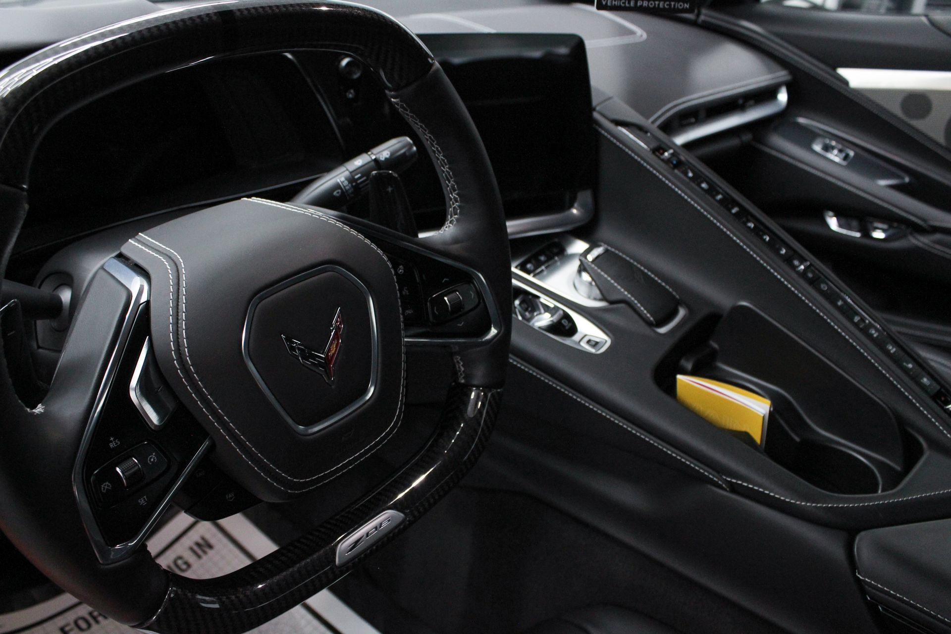 A close-up interior view of a black Chevrolet Corvette cockpit with a leather-wrapped steering wheel and center console.