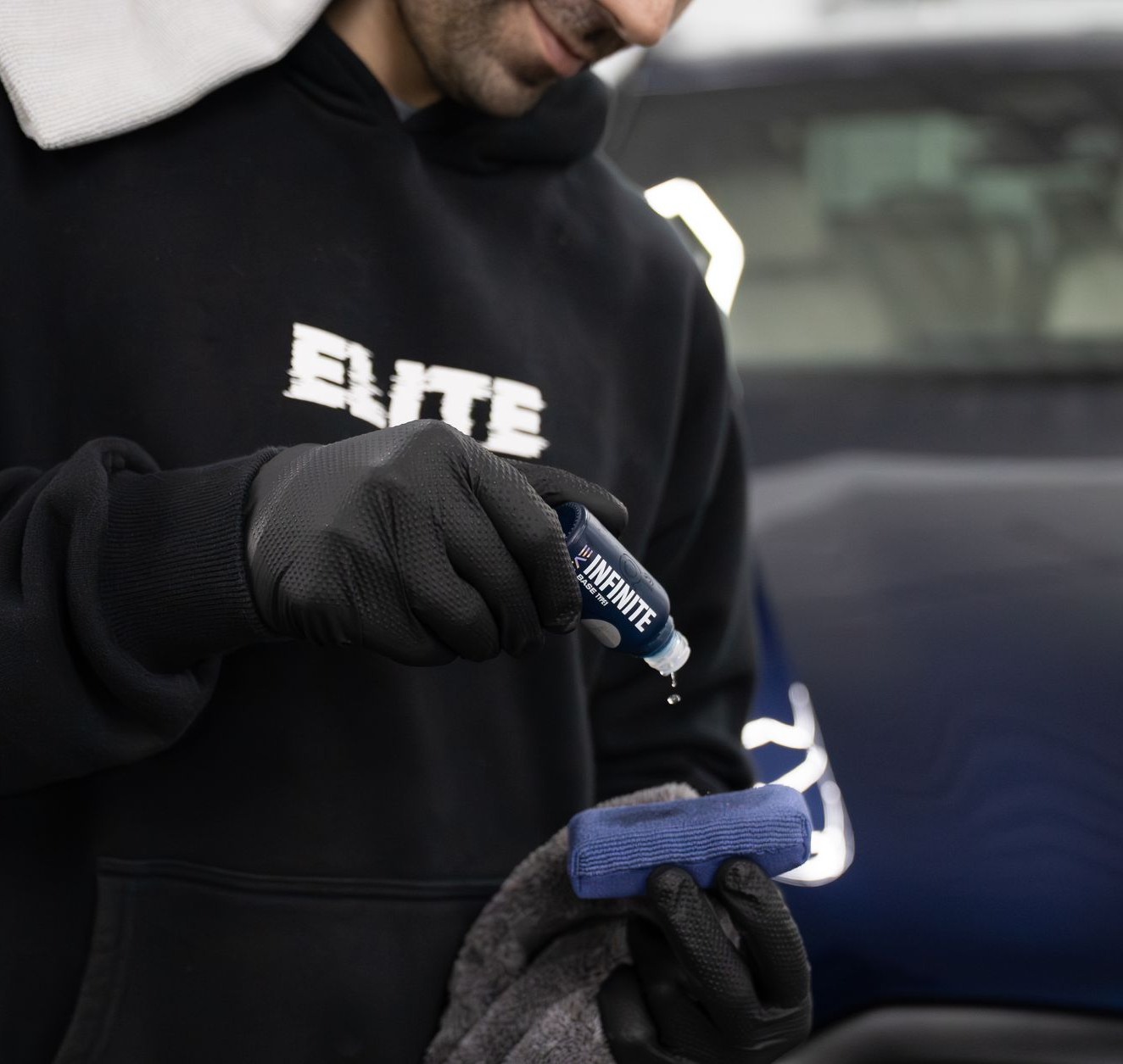 A person is cleaning a car with a towel and gloves.