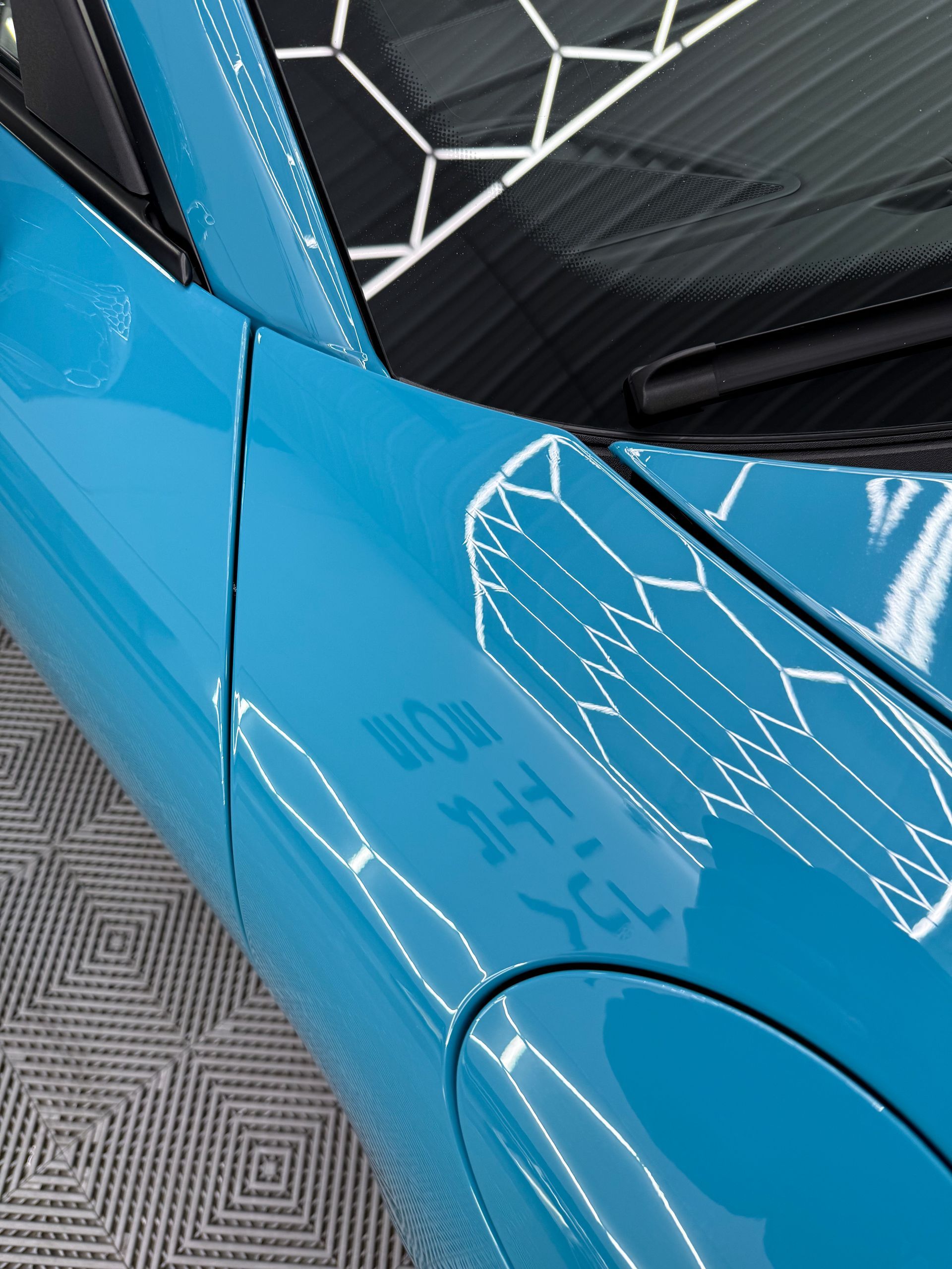 A man is wrapping a blue car in a garage.