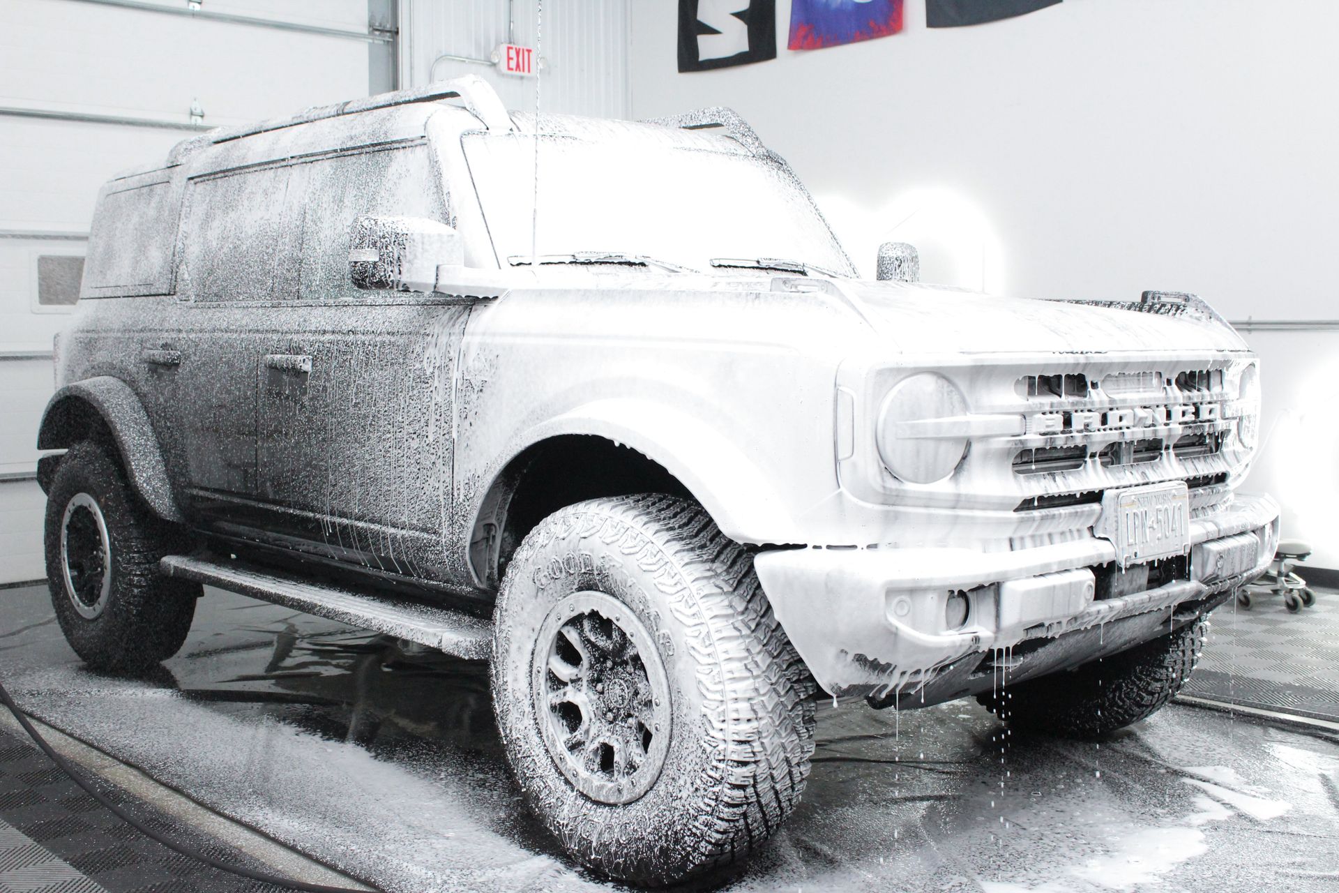 A Ford Bronco covered in thick white soap suds during an indoor car wash.