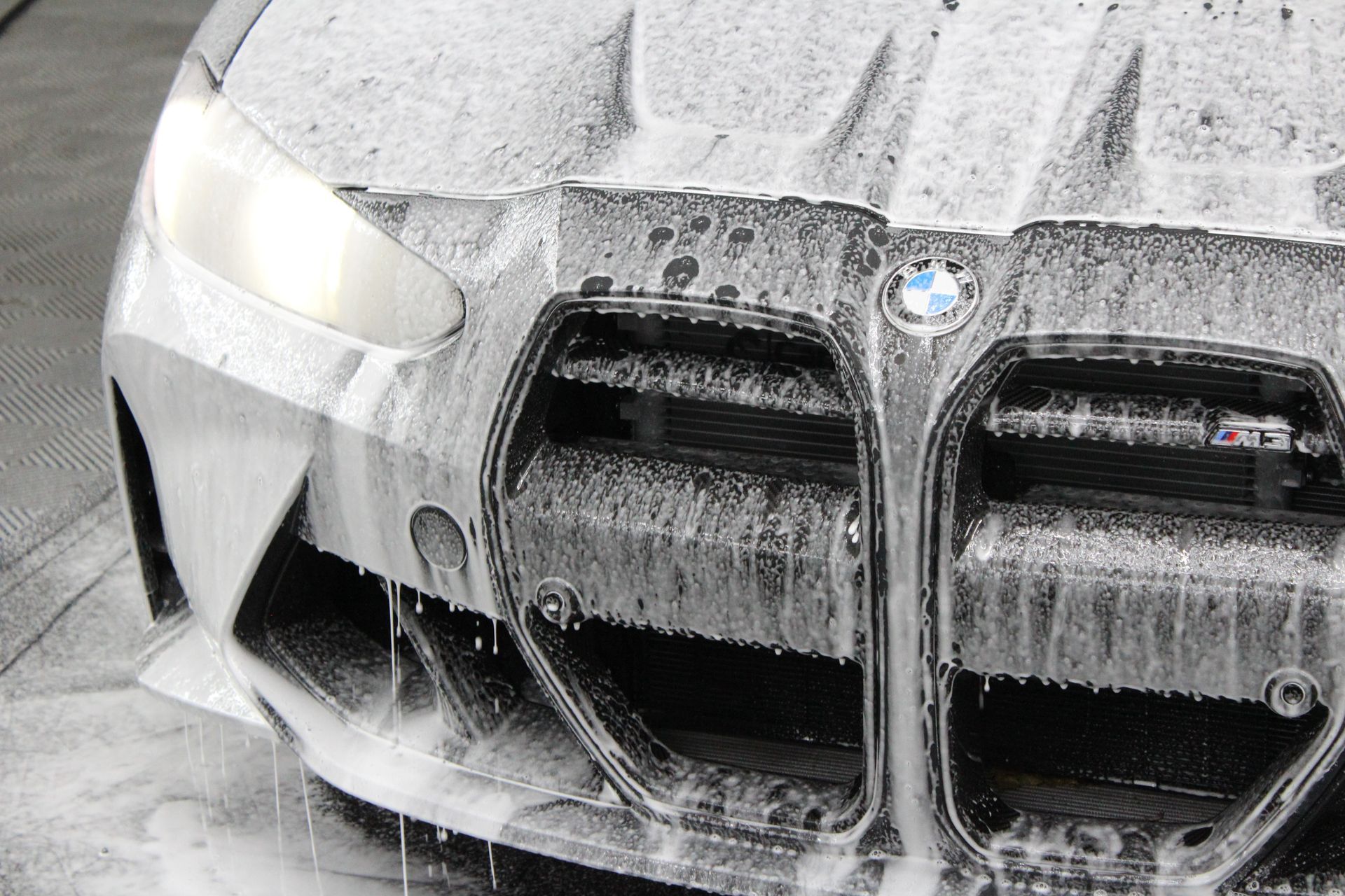 A close-up view of the front of a BMW covered in thick white car wash soap.
