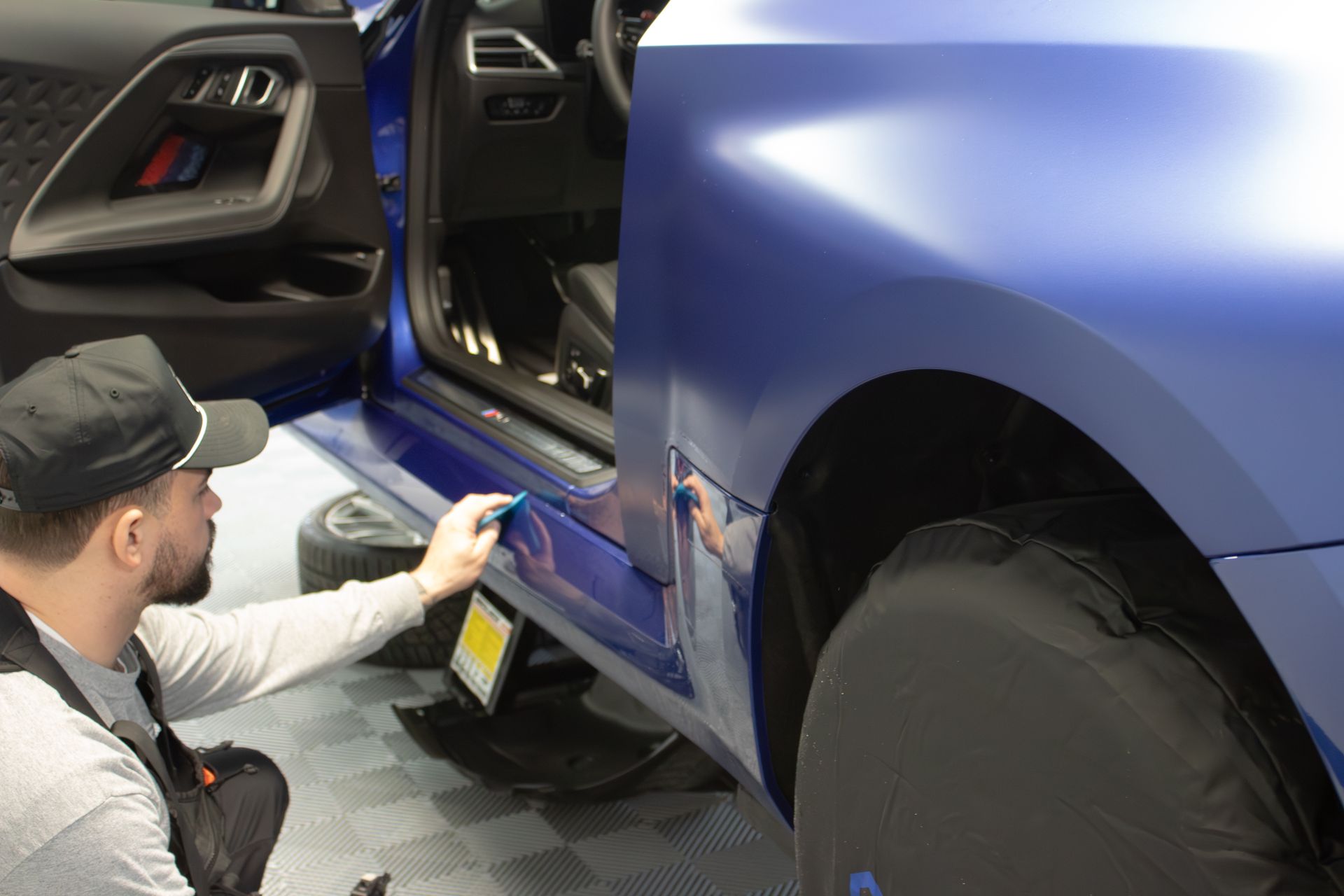 A person is applying a clear film to a black car hood.