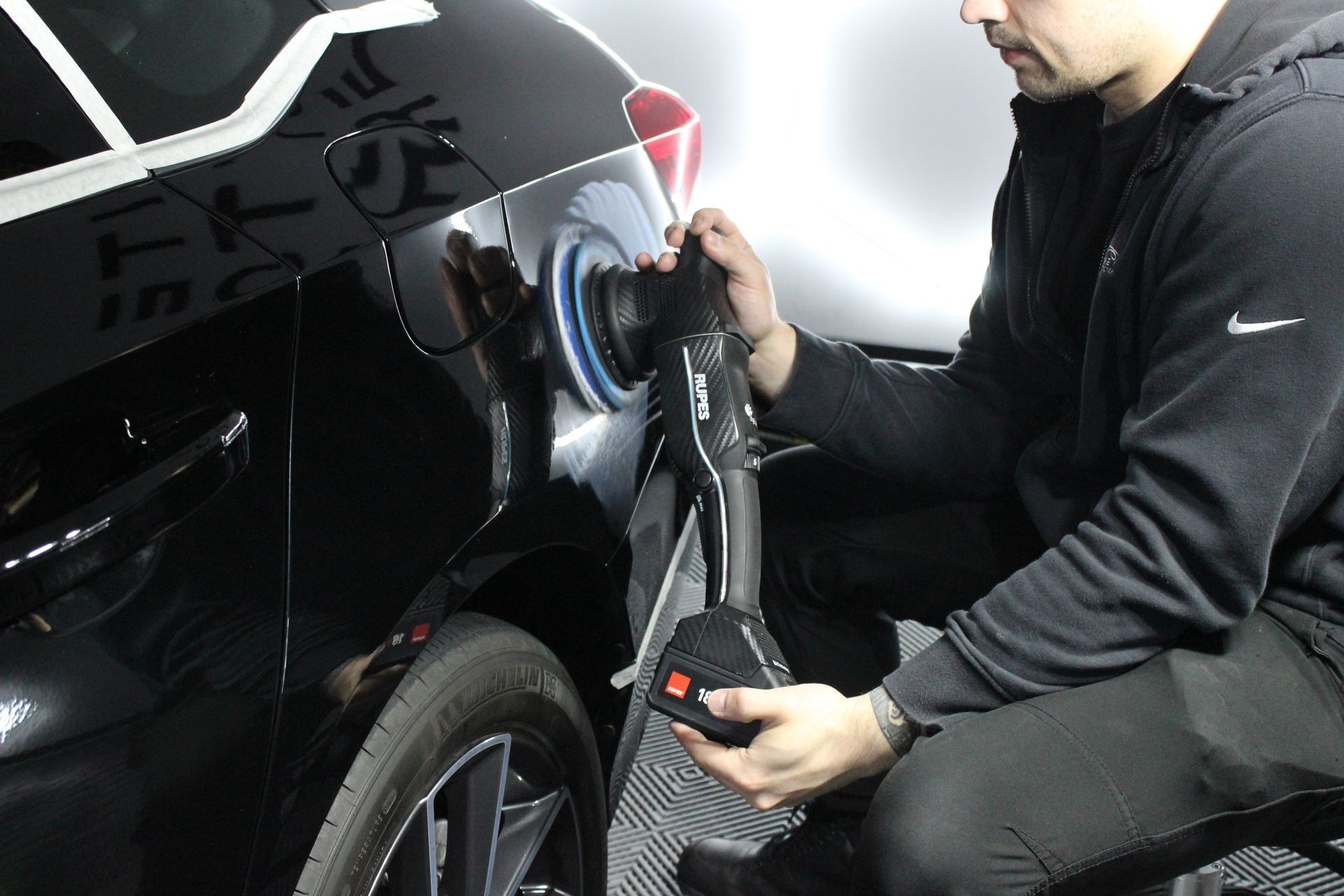 A man is polishing a red car with a polisher.