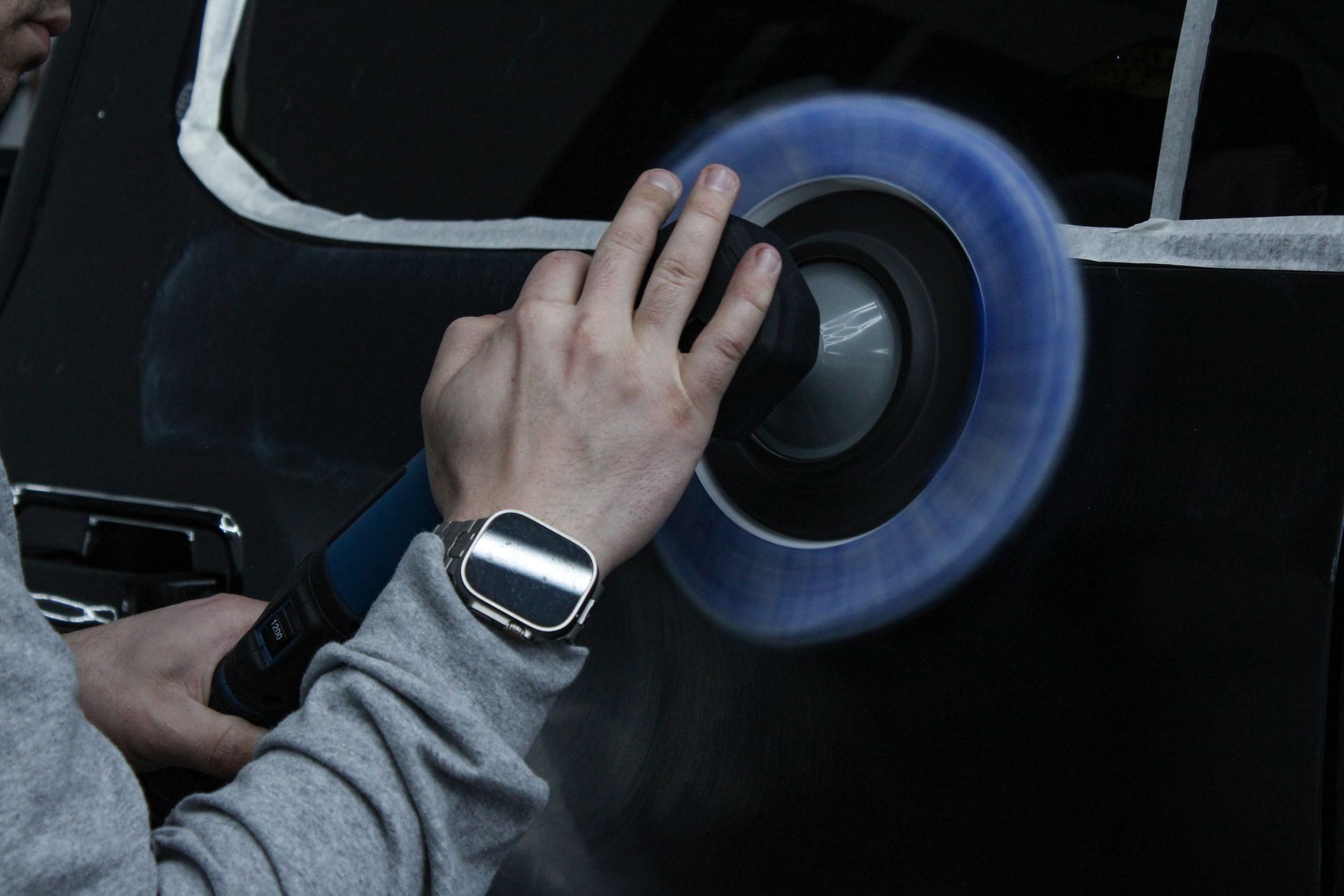 A person is polishing the back of a blue car