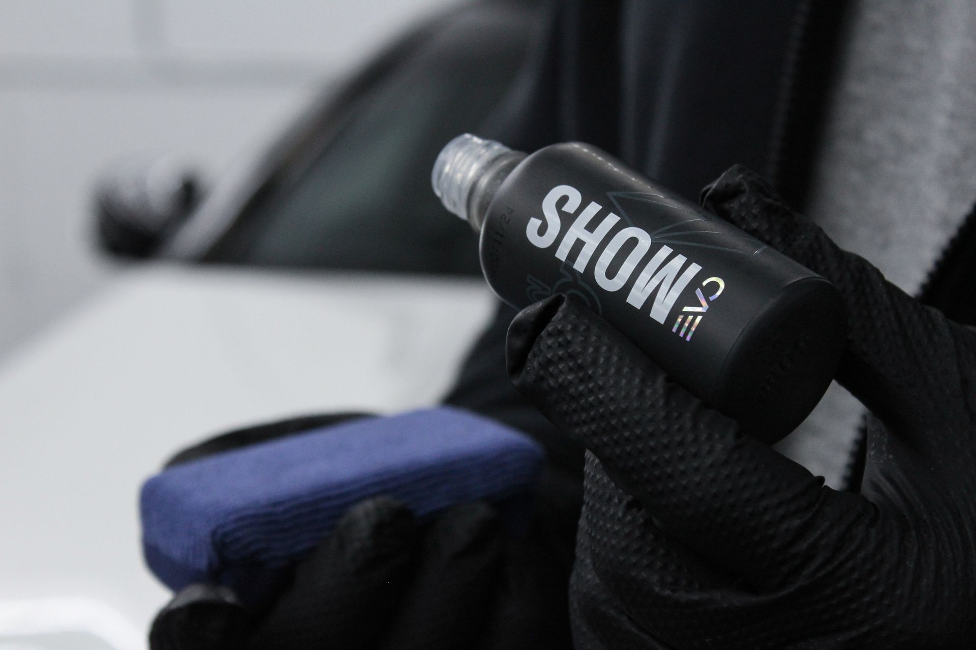 Hands in black gloves holding a ceramic coating bottle labeled 
