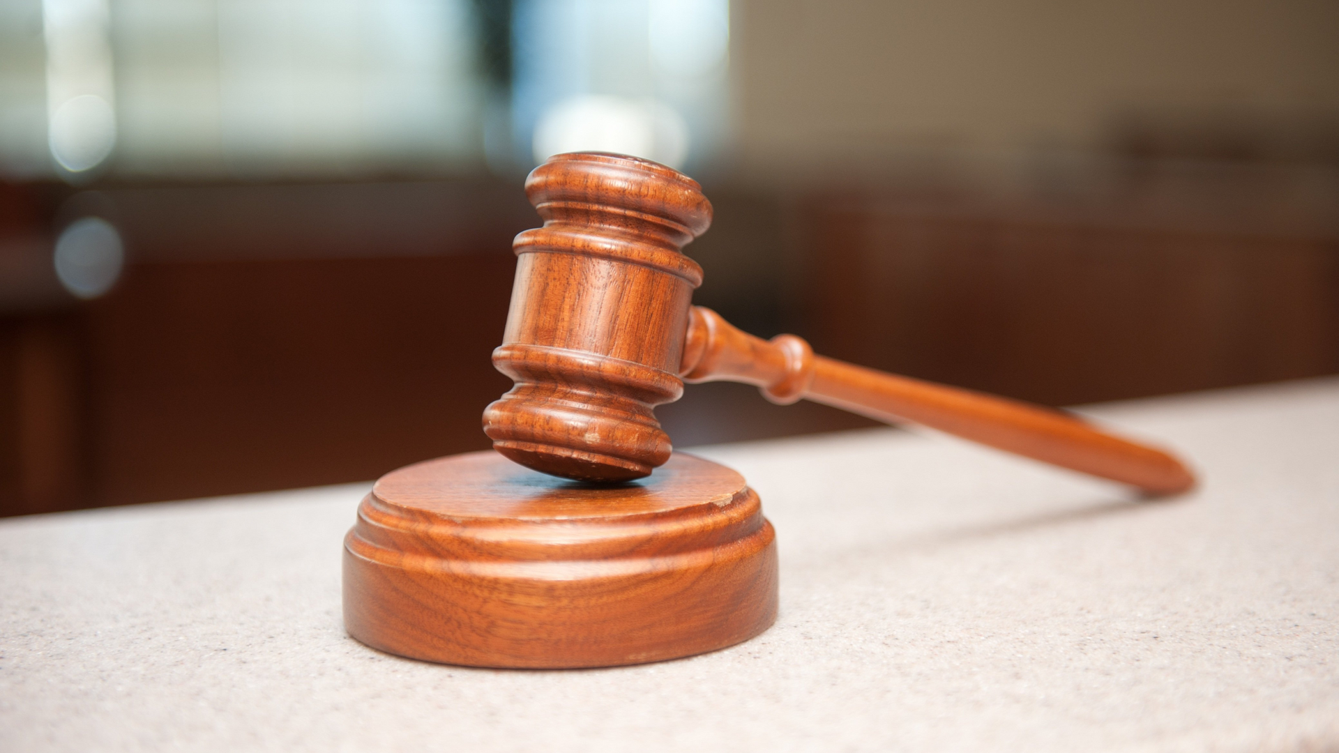 Wooden gavel on a round wooden base, on a light-colored surface with a blurred background.