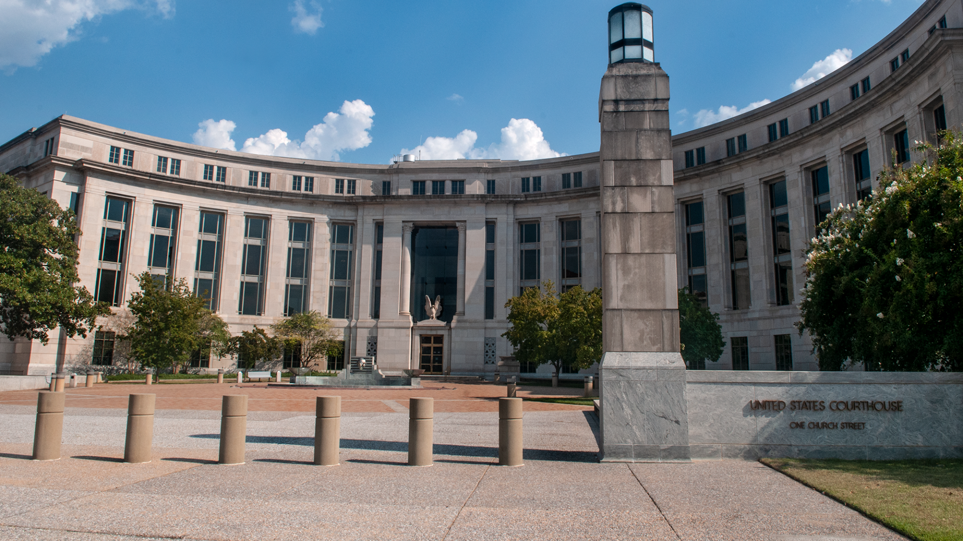 Curved building with many windows, tall pillar, nameplate
