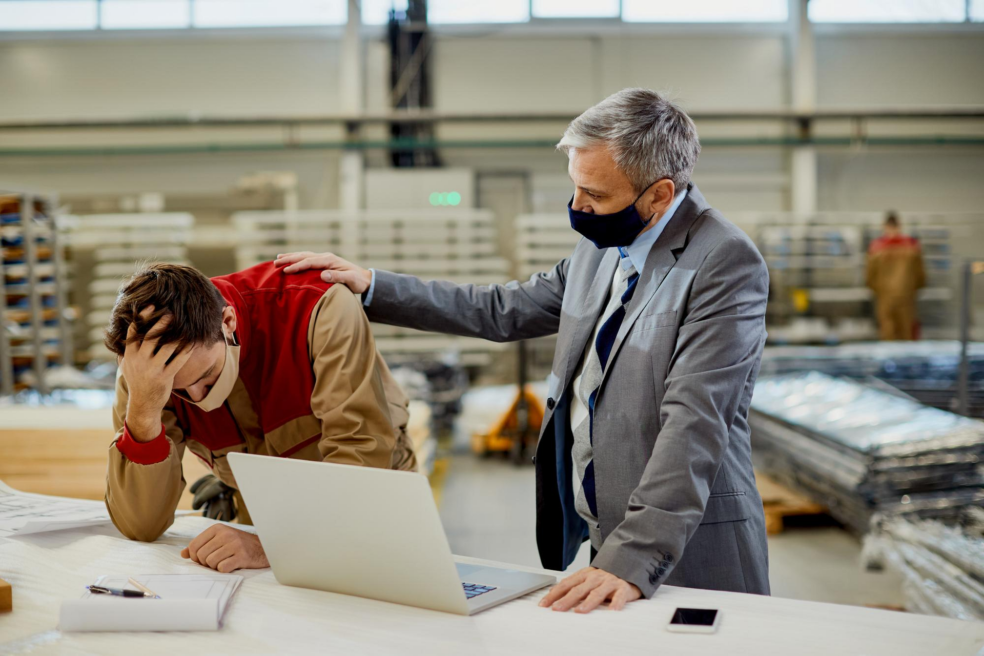 Concerned manager speaking with and supporting a stressed employee in an industrial workplace after